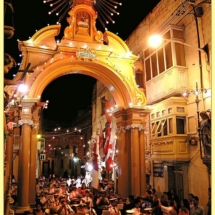 A band procession through a triumphal arch erected for the village feast